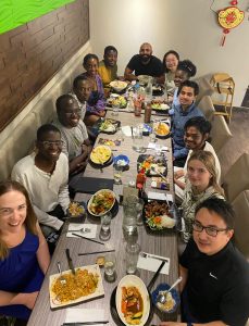 Adriana Velibekova takes a group photo with her friends at a restaurant and they are all sat down with food in front of them and there are lots of people at the table.