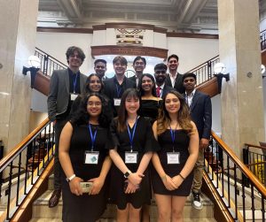 Teresa and her friends take a pictures on a stairway. Everyone is dressed up formally and in black with a lanyard around their neck.