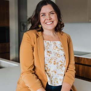 Catherine Melville sits on a white counter and is dressed in semi-formal clothes. 